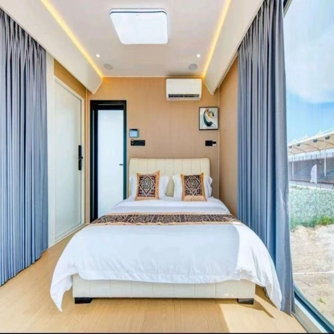 It's a prefabricated house with large glass windows and a comfortable double bed